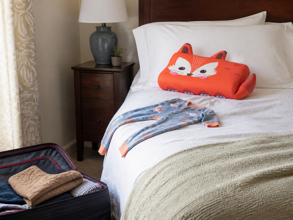 RYVA fox pillow on a hotel bed next to an open suitcase